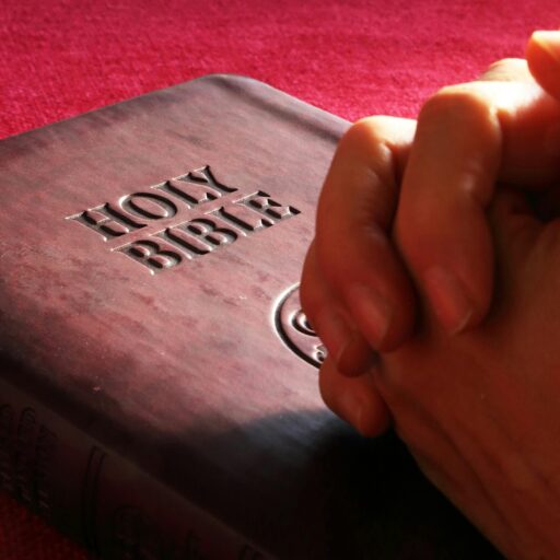 Close-up of hands praying on a Holy Bible, symbolizing faith and spirituality.